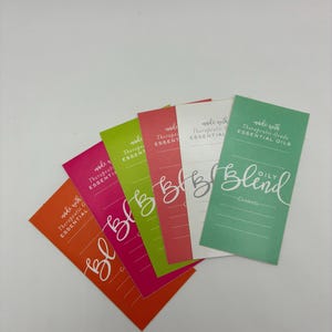 May include: A selection of vibrant rectangular product labels in orange, pink, green, and white. Each label displays the text "made with Therapeutic Grade ESSENTIAL OILS" and the word "Blind" in a script font. The labels are arranged in a fan shape.