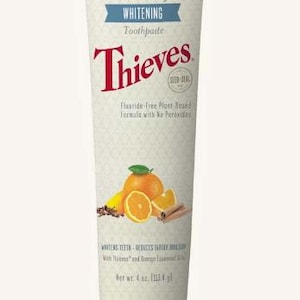 Puede incluir: Un tubo de pasta dental blanqueadora Thieves. El tubo es blanquecino con texto y gráficos. El texto incluye "Essential Oil-Infused Whitening Toothpaste" y "Thieves". Los gráficos incluyen naranjas, palitos de canela y clavos. El tubo contiene 113,4 g.