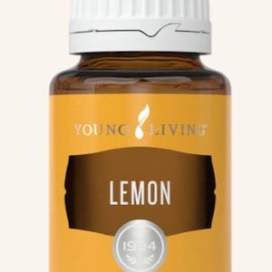 Op de afbeelding: Een bruine glazen fles Young Living Lemon essentiële olie. De fles heeft een witte dop en een geel etiket met het woord "LEMON" en "1994" erop gedrukt. De fles bevat 15 ml olie.