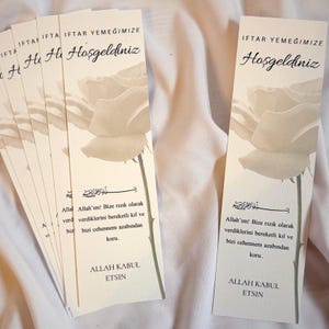 Könnte beinhalten: Cremefarbene Lesezeichen mit einer Rosenillustration und türkischem Text. Die Lesezeichen tragen die Worte "IFTAR YEMEĞIMIZE Hoşgeldiniz" und religiösen Text. Die Lesezeichen sind fächerförmig angeordnet.