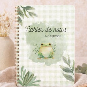 Peut inclure: Cahier de notes à spirales avec un motif à carreaux verts et blancs. La couverture présente une illustration de grenouille et les mots "Cahier de notes" et "Notebook". Des feuilles vertes ornent le design.