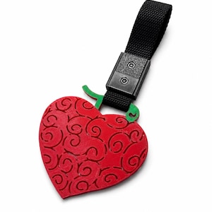 Puede incluir: Un llavero rojo con forma de corazón que presenta un patrón de remolinos texturizados y un tallo verde. El corazón está unido a una correa de tela negra mediante un clip de plástico negro con dos remaches plateados, creando un accesorio.