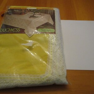 May include: A yellow Duchess tablecloth in its original packaging, featuring a white lace trim. The packaging shows a picture of the tablecloth on a table. The tablecloth measures 60 x 84 inches.