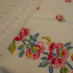 Pu&ograve; includere: Tessuto bianco con un bordo floreale a punto croce in rosso, rosa, giallo e blu. Il disegno presenta un motivo floreale ripetuto. &Egrave; visibile un pezzo separato di tessuto bianco con dettagli traforati.