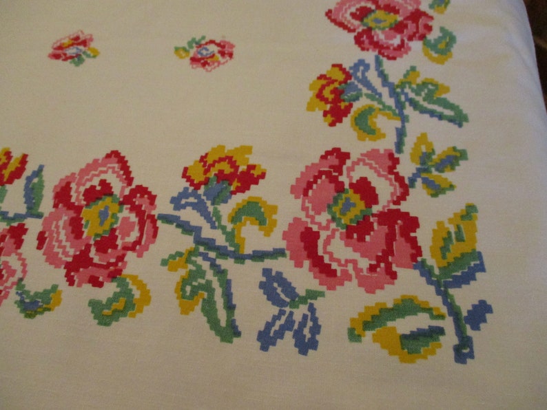 Pu&ograve; includere: Tovaglia bianco sporco con un motivo floreale a punto croce. I fiori sono nelle tonalit&agrave; del rosa, rosso, giallo e blu, con foglie verdi. Il disegno &egrave; sul bordo e negli angoli della tovaglia.