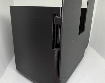 May include: A black 3D-printed plastic enclosure featuring a hinged side panel and a rectangular cutout on the front face. The structure has a smooth, matte finish with visible layer lines from the manufacturing process and a vertical hinge mechanism.
