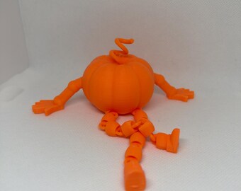 May include: A bright orange 3D printed pumpkin figurine featuring a round, ribbed body with a curly stem on top. The pumpkin has articulated arms with five-fingered hands and jointed legs with feet, allowing it to sit in a pose.