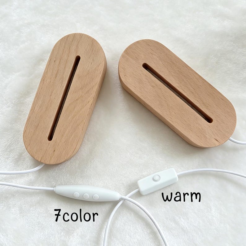 May include: Two oval-shaped light-colored wooden display bases with a central slot for inserts. Each base features a white power cord. One cord includes a controller with three buttons labeled 7color, and the other has a switch labeled warm.