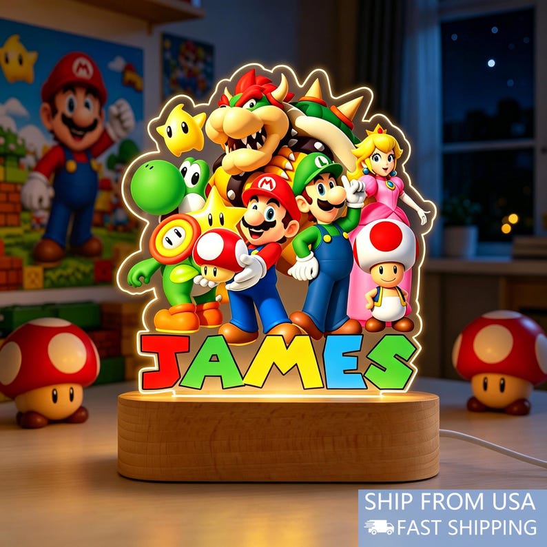 May include: An illuminated acrylic night light featuring a colorful graphic of Mario, Luigi, Princess Peach, Bowser, Yoshi, and Toad. The name JAMES is printed in large, multi-colored block letters at the base, set on a smooth wooden stand.