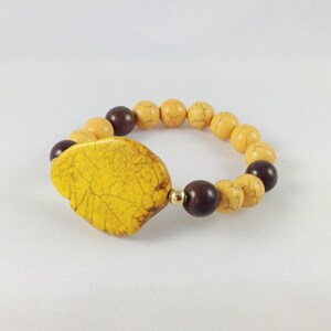 May include: A yellow and brown beaded bracelet with a large yellow stone charm. The bracelet is made of natural stones and has a simple design.