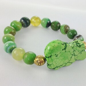 May include: A green and yellow agate bead bracelet with a large green howlite charm and gold accents.