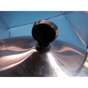 May include: A polished stainless steel lid featuring a smooth, reflective surface and a centered, rounded black knob handle. The metallic dome shape captures light across its curved exterior, providing a clear view of the lid's finish.
