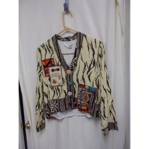 May include: A long-sleeve button-up jacket featuring a cream base with a black zebra-like print. The garment includes contrasting patchwork panels in orange, blue, and black geometric patterns, finished with round buttons and a V-neckline.