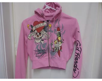 May include: A light pink zip-up hoodie featuring a graphic of a skull with a heart banner reading LOVE KILLS SLOWLY, a dagger, and the text DON ED HARDY DESIGNS. The left sleeve features the text ED HARDY in black script lettering on the fabric.