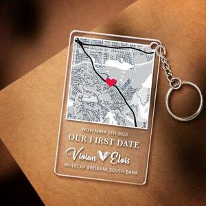 May include: Clear acrylic keychain featuring a map with a red heart marking a location. The text reads "November 9th 2023, Our First Date, Vivian & Elvis, Wheel of Brisbane, South Bank". Includes a silver chain and keyring.