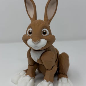 May include: A brown and white rabbit figurine with large ears and expressive eyes. The rabbit is in a seated position, with its front paws and chest in white. The figurine has a friendly, cartoonish appearance.