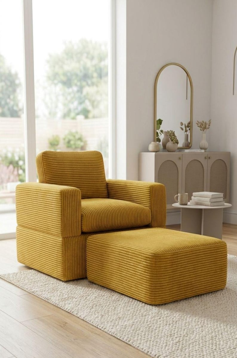 K&ouml;nnte beinhalten: Senfgelber Cord-Sessel mit passendem Hocker. Der Sessel hat eine quadratische Form mit gepolstertem Sitz, R&uuml;ckenlehne und Armlehnen. Der Hocker ist rechteckig. Das Set steht auf einem cremefarbenen Teppich in einem hellen Raum.