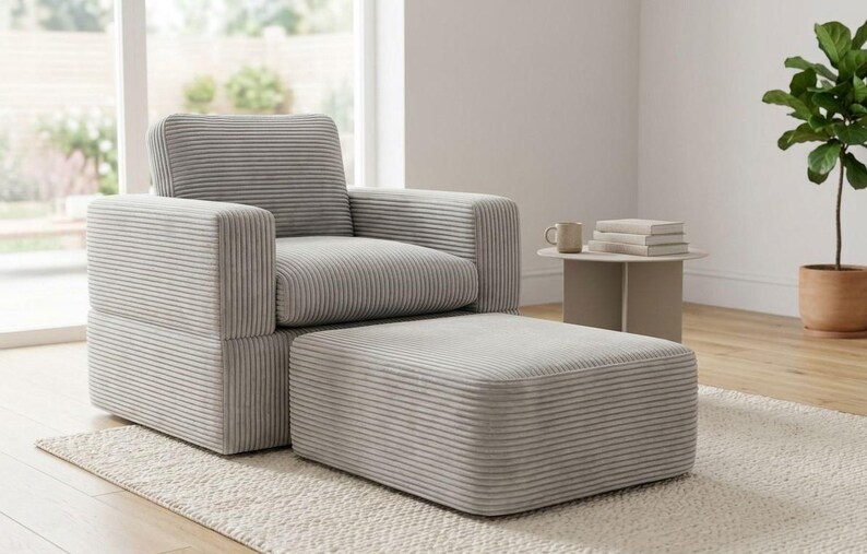 K&ouml;nnte beinhalten: Ein hellgrauer Cord-Sessel und eine passende Fu&szlig;st&uuml;tze. Der Sessel hat eine quadratische Form mit gepolstertem Sitz, R&uuml;ckenlehne und Armlehnen. Die Fu&szlig;st&uuml;tze ist rechteckig.