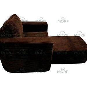 K&ouml;nnte beinhalten: Ein braunes Cord-Ecksofa mit angebauter Ottomane. Das Sofa hat ein abgerundetes Design mit einem dicken, strukturierten Stoff. Die Ottomane ist rechteckig und passt farblich und materialm&auml;&szlig;ig zum Sofa. Das Sofa steht vor wei&szlig;em Hintergrund.