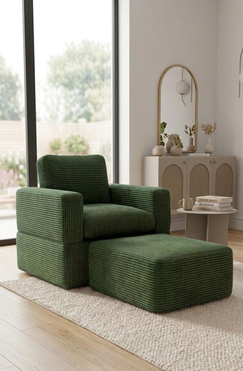 K&ouml;nnte beinhalten: Ein gr&uuml;ner Cord-Sessel mit passendem Hocker steht auf einem cremefarbenen Teppich. Der Sessel hat eine kastenf&ouml;rmige Form mit hoher R&uuml;ckenlehne und Armlehnen. Ein gro&szlig;es Fenster und ein dekorativer Spiegel sind im Hintergrund.