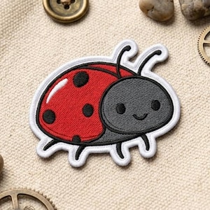 May include: A beige canvas bag with a red and black ladybug patch, a gold button, two small stones, and two small metal gears. The ladybug patch has a smiling face and is surrounded by a white border.