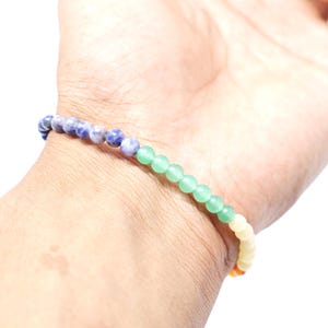 May include: A beaded bracelet with a rainbow color scheme. The bracelet features small, round beads in shades of blue, green, yellow, and orange. The bracelet is worn on a wrist, showcasing the vibrant colors and design.