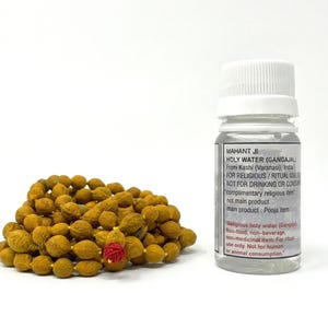 May include: A clear plastic bottle with a white cap and text reading "Holy Water" sits next to a strand of brown prayer beads with a red accent. The bottle contains a clear liquid.