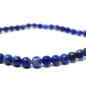 May include: A delicate bracelet featuring small, round, deep blue lapis lazuli beads. The beads are strung together, creating a flexible, elegant accessory. The bracelet is set against a plain white background.
