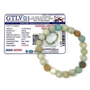 May include: A natural Amazonite bracelet with pale green beads. The bracelet is strung and features a variety of colors, including white, tan, and blue-green. A gemstone identification report is visible in the background.