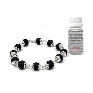 May include: A black beaded bracelet with silver-colored accents and a small bottle with white text. The bracelet features round, matte black beads separated by ornate silver-toned connectors. The bottle has a white cap and a label with black text.