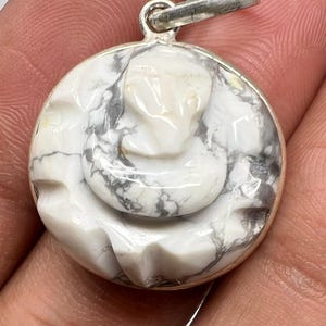 May include: A round pendant with a white and gray marbled stone design. The pendant has a silver-colored bail and a carved floral or abstract design. The stone has a polished, glossy finish.