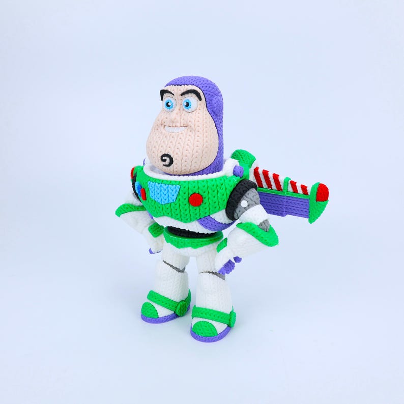 May include: A crocheted Buzz Lightyear figure featuring a purple hood, a white, green, and purple spacesuit with red and blue circular accents, and a pair of wings with red and white diagonal stripes on the back, all crafted with yarn.