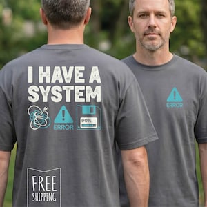 May include: Two gray t-shirts with the text "I HAVE A SYSTEM" and graphics on the back, including a tangled cord, an exclamation point, and a floppy disk. The front of one shirt has an exclamation point symbol and the word "ERROR".