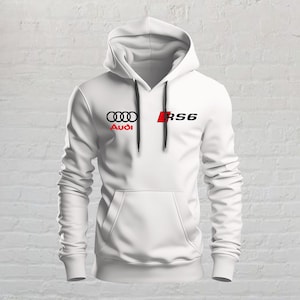 May include: A white long-sleeve hooded sweatshirt featuring a front kangaroo pocket and black drawstring cords. The chest displays the black Audi four-ring logo with the red Audi text below it, alongside a red square with the black text RS6.
