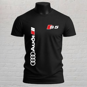 May include: A black short-sleeved t-shirt featuring a vertical white Audi logo with a red accent block on the left side and a white S5 logo with a red square accent on the upper right chest area. The shirt has a crew neckline and a standard fit.