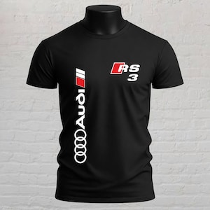May include: A black short-sleeved t-shirt featuring a vertical white Audi logo with a red accent stripe on the left side and the white and red RS 3 logo positioned on the upper right chest area, displayed on a mannequin torso.