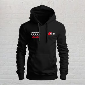 Può includere: Una felpa nera con cappuccio che presenta il logo Audi bianco con la scritta Audi rossa sottostante sul petto sinistro e un logo RS rosso e bianco sul petto destro. Il capo include una tasca a marsupio frontale e lacci neri abbinati.