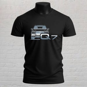 May include: A black short-sleeved t-shirt featuring a graphic print of a silver Audi Q7 vehicle on the front chest. The design includes the front view of the car with the text Q7 displayed in a bold, metallic-style font next to the vehicle.