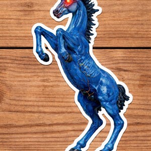 May include: A blue sticker of a rearing horse with glowing red eyes. The horse has a dark mane and tail, and a detailed, textured appearance. The sticker is on a wooden background.