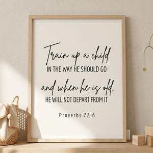 Può includere: Una stampa incorniciata con la scritta "Train up a child in the way he should go and when he is old, he will not depart from it. Proverbs 22:6" in corsivo nero. La cornice è marrone chiaro, con sfondo bianco sporco.