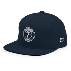 Può includere: Un berretto da baseball blu navy con visiera piatta. Il berretto presenta un testo ricamato bianco e un logo sul davanti che recita "7th INNING STYLE" attorno a un numero 7 bianco. Il lato del berretto ha un logo "7th" bianco.