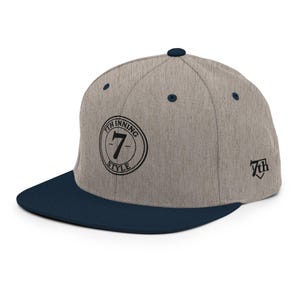 Può includere: Cappellino da baseball con corona grigia e visiera blu navy. Il cappellino presenta la scritta "7th Inning Style" in un cerchio sul davanti, con il numero "7" all'interno. Il lato del cappellino riporta la scritta "7th" in un carattere stilizzato.
