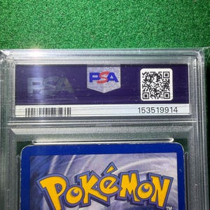May include: A graded Pok&eacute;mon trading card encased in a clear plastic holder. The card's back features the Pok&eacute;mon logo in yellow and orange against a blue background. The holder has a PSA label with a QR code and serial number.