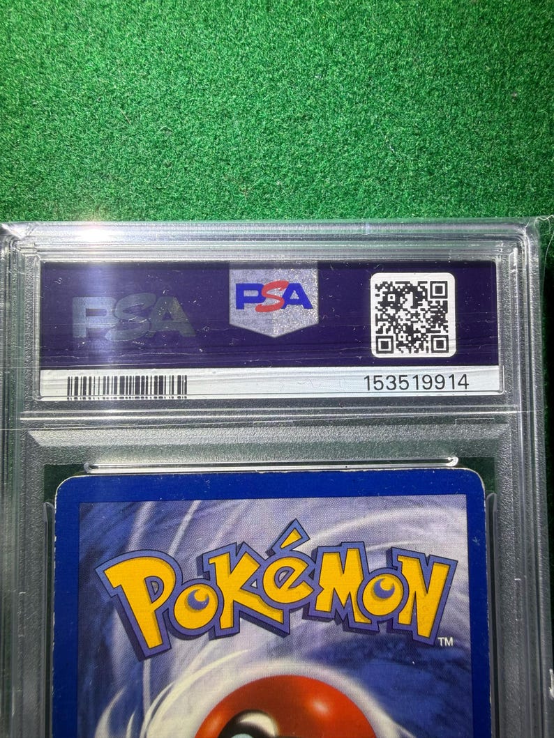 May include: A graded Pok&eacute;mon trading card encased in a clear plastic holder. The card's back features the Pok&eacute;mon logo in yellow and orange against a blue background. The holder has a PSA label with a QR code and serial number.