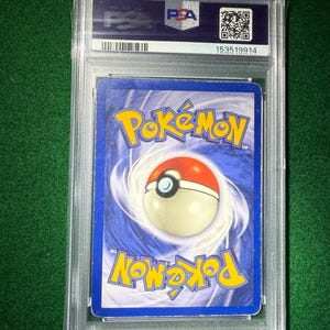 May include: A graded Pok&eacute;mon trading card encased in a clear plastic holder. The card's back features a blue background with the Pok&eacute;mon logo and a Pok&eacute; Ball design. The holder has a PSA label with a barcode and QR code.