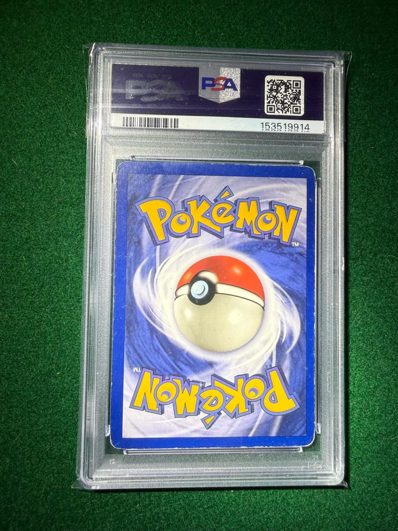 May include: A graded Pok&eacute;mon trading card encased in a clear plastic holder. The card's back features a blue background with the Pok&eacute;mon logo and a Pok&eacute; Ball design. The holder has a PSA label with a barcode and QR code.