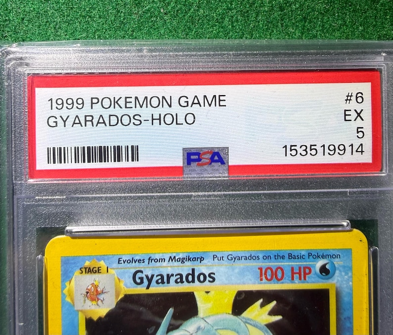 May include: A graded Pok&eacute;mon card featuring Gyarados, a Stage 1 Pok&eacute;mon. The card is encased in a clear plastic holder with a red label that reads "1999 Pokemon Game Gyarados-Holo". The card is graded EX 5.