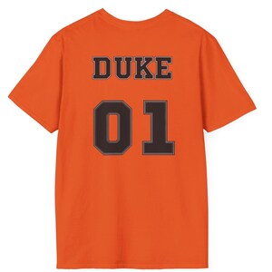 May include: A bright orange short-sleeved t-shirt featuring the word DUKE in black block letters above the large black number 01. The text and number are centered on the back of the shirt, displaying a bold, high-contrast design.