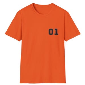 May include: A bright orange short-sleeved t-shirt featuring a crew neckline. The front of the garment displays the number 01 printed in a bold, dark, block-style font on the upper left chest area, providing a clear contrast to the fabric.