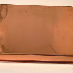 May include: A rectangular copper serving tray with rounded corners and two brass handles attached to the sides. The surface of the tray is smooth and metallic with a warm reddish-brown tone, showing minor surface scratches and light reflections.